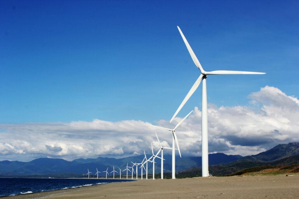 pexels-photo-3976320-3976320 A row of wind turbines on a sandy coastline under a clear blue sky, promoting renewable energy.